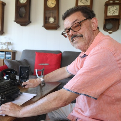 Peter Hennes sitzt an einem Schreibtisch, auf dem eine alte Rechenmaschine steht.