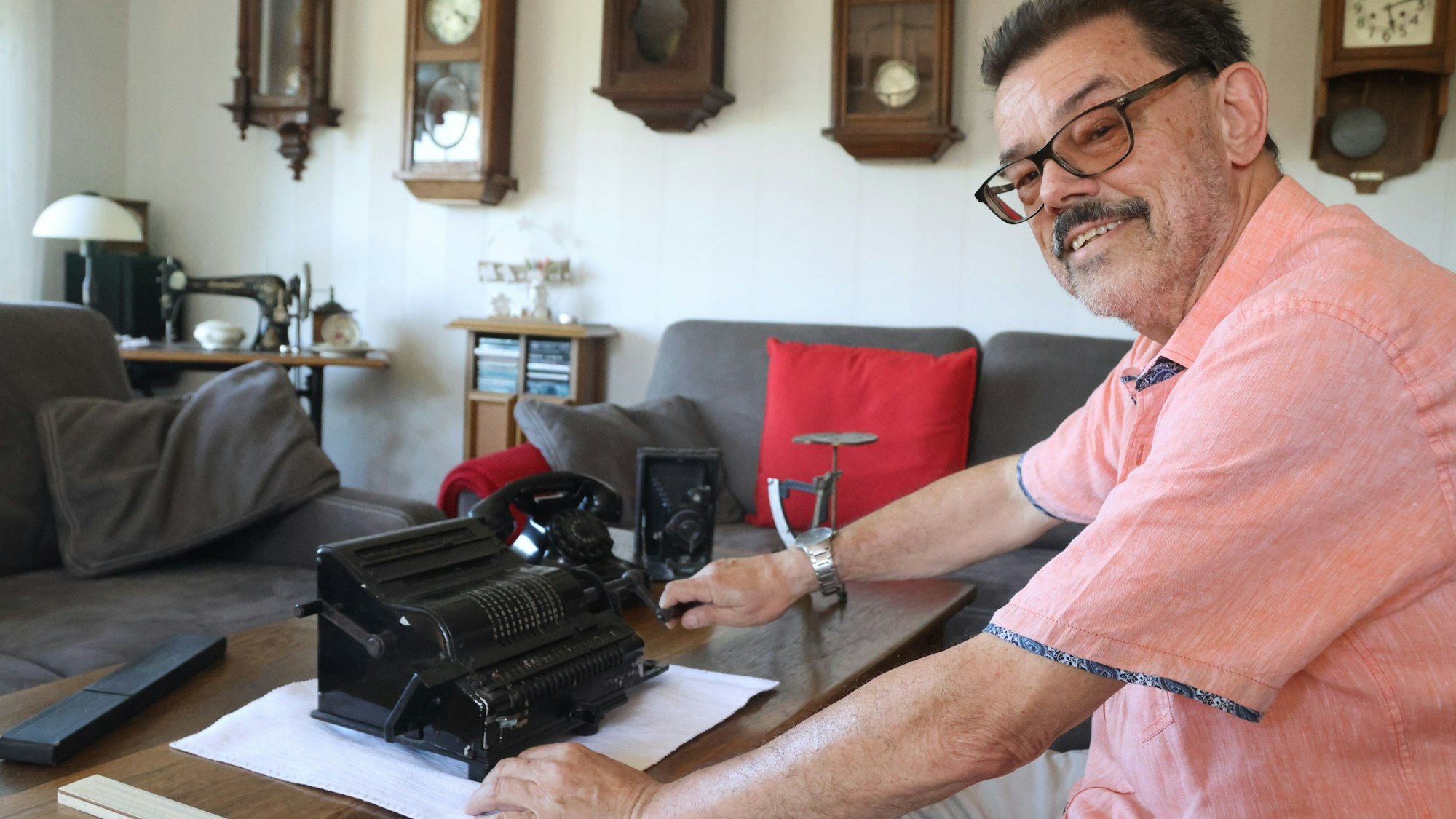 Peter Hennes sitzt an einem Schreibtisch, auf dem eine alte Rechenmaschine steht.