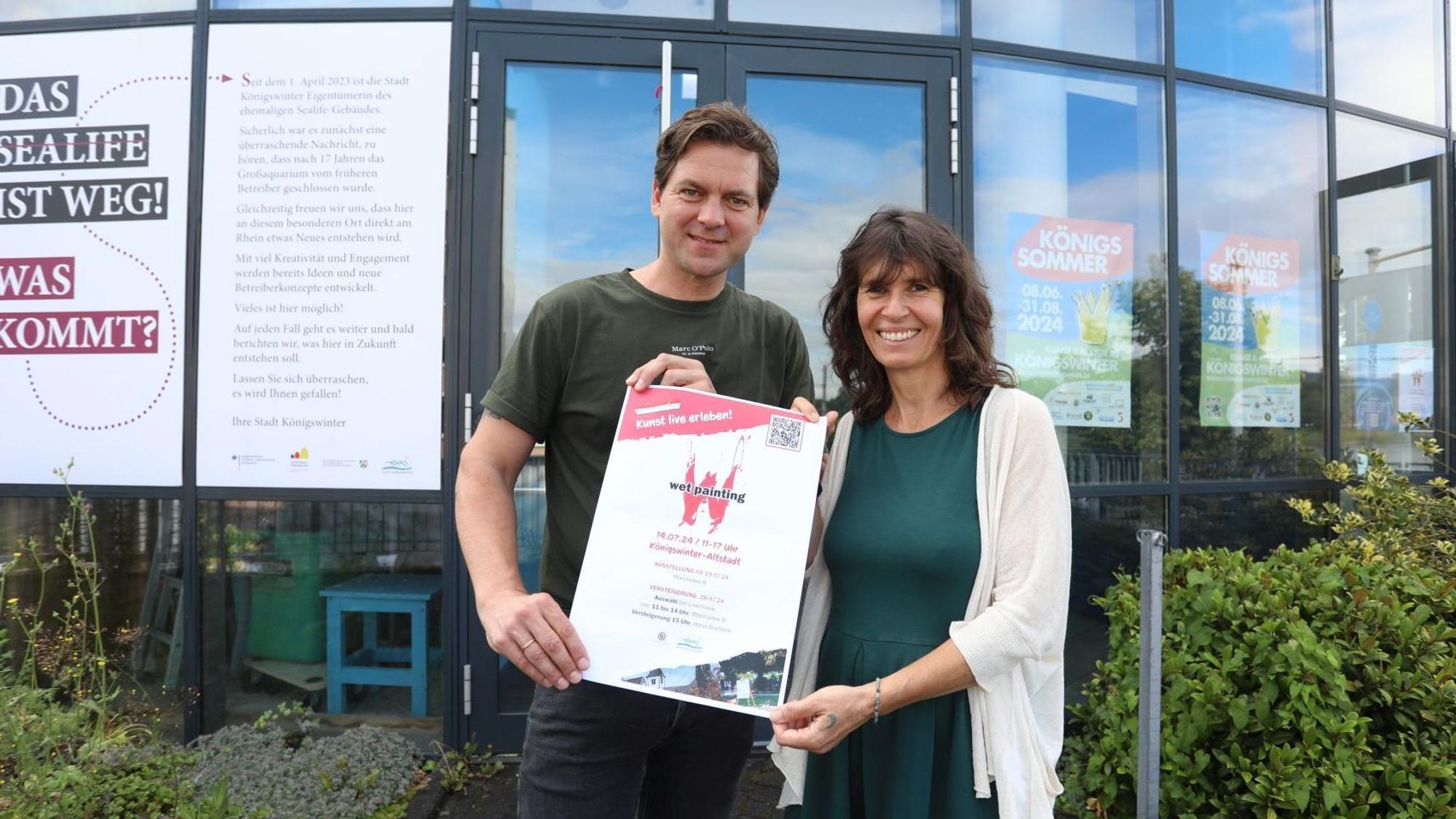Ein Mann und eine Frau halten ein Plakat in den Händen.