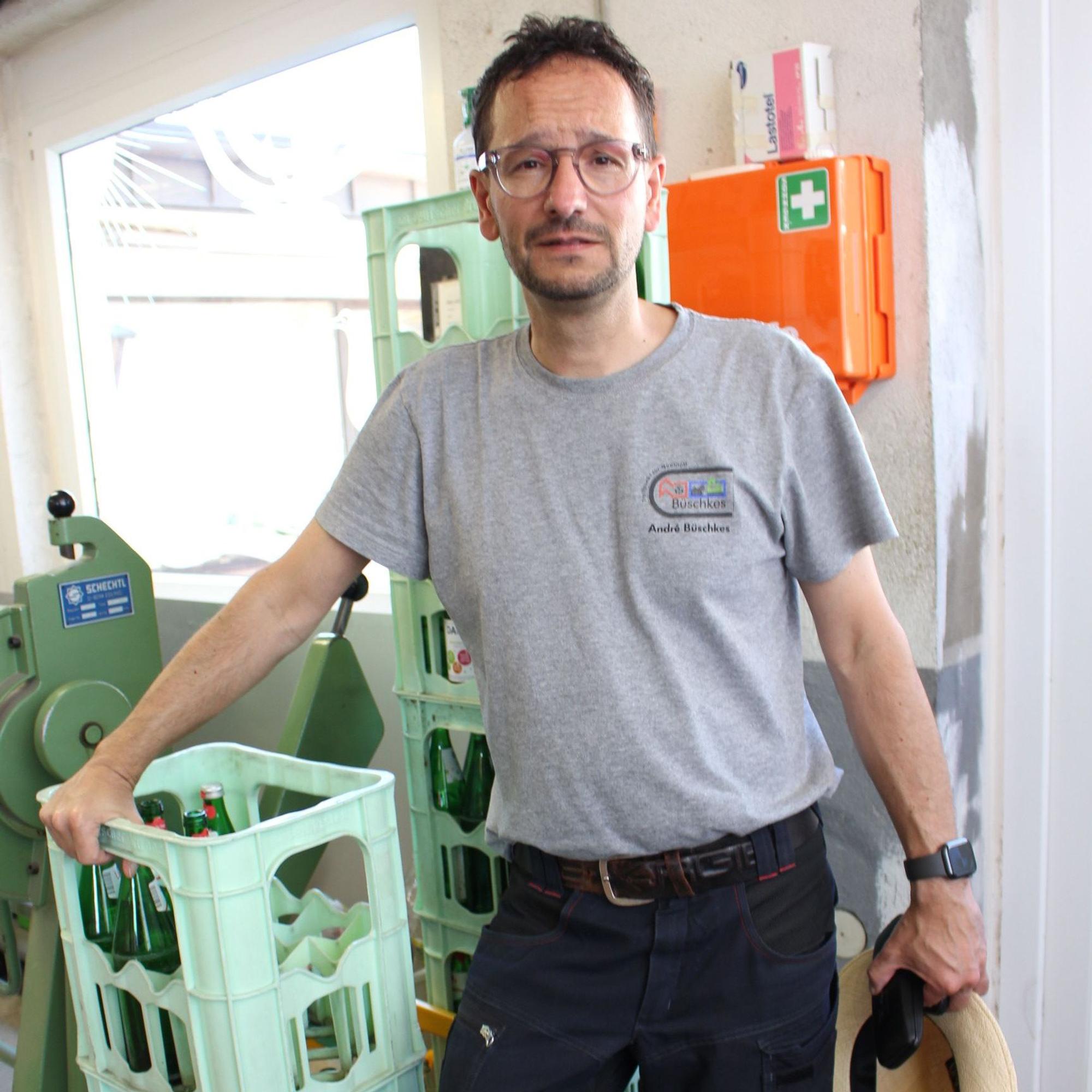 Ein lehnt in grauem Poloshirt und dunkler Arbeitshose gegen mehrere hellgrüne Wasserkästen.
