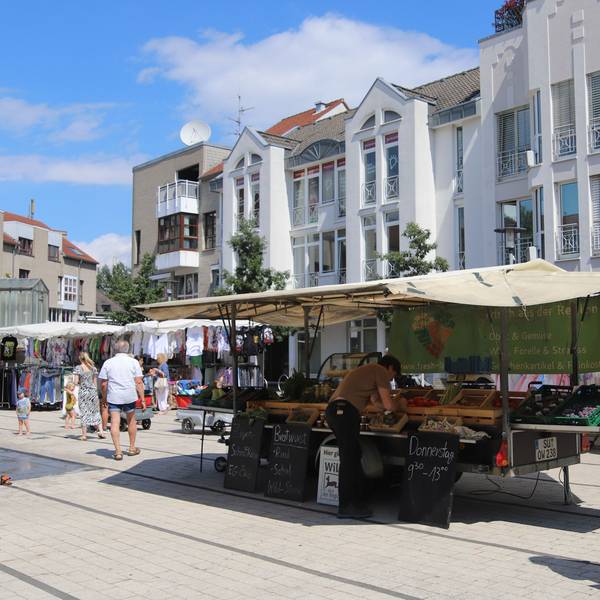 Marktstände mit Obst und Kleidung auf dem Hennefer Marktplatz, eine Frau mit Einkaufstasche geht vorbei.