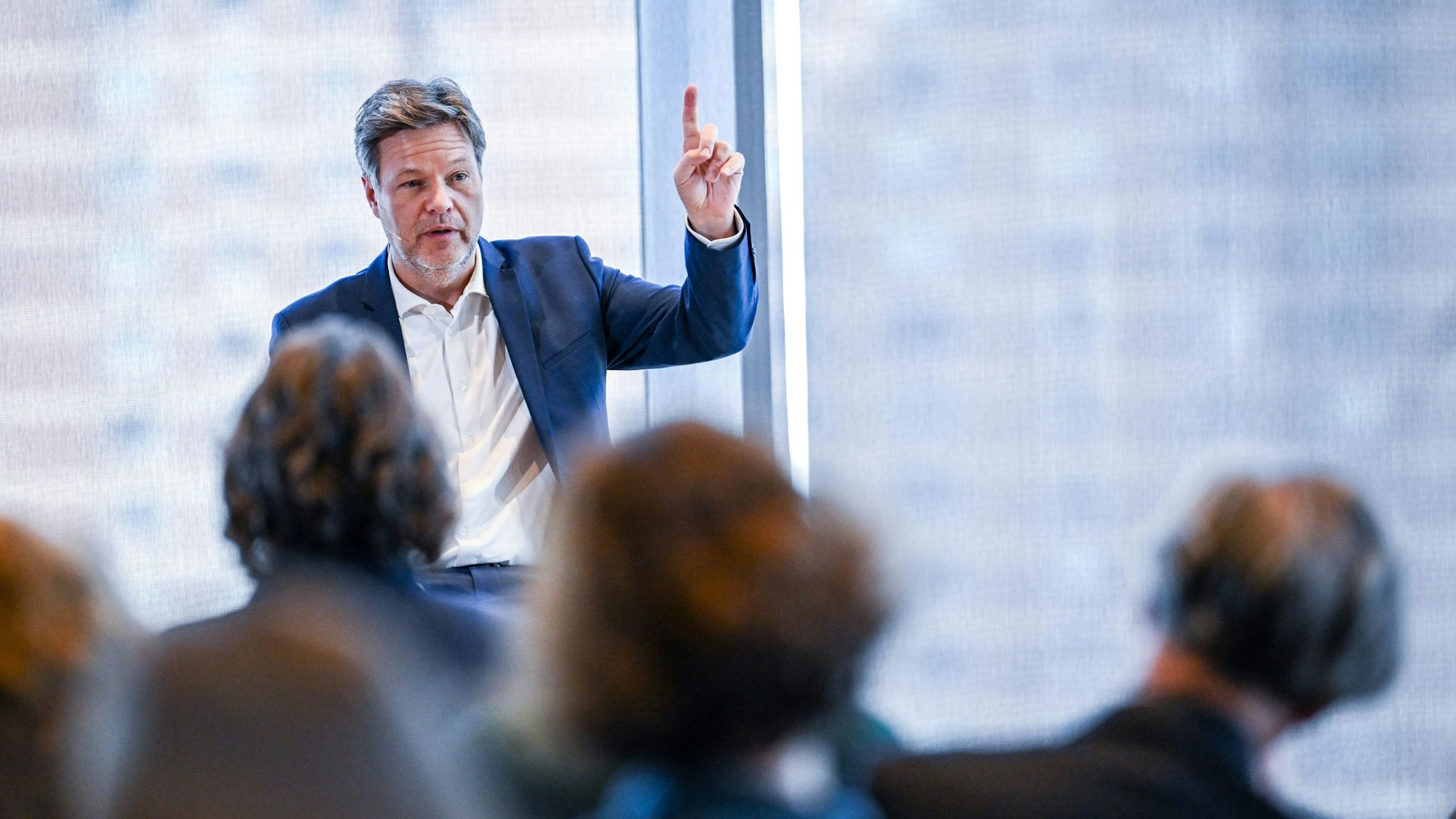 Robert Habeck sitzt vor mehreren Personen und hebt den Finger.