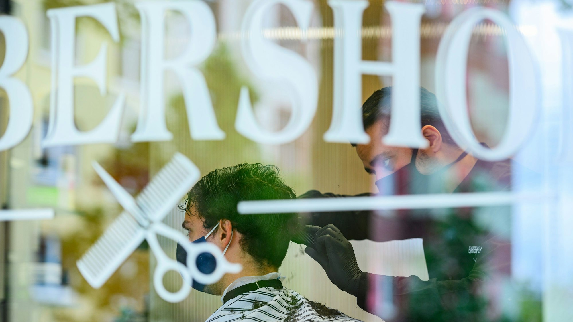Ein Friseur schneidet in einm Barbershop einem Kunden die Haare.