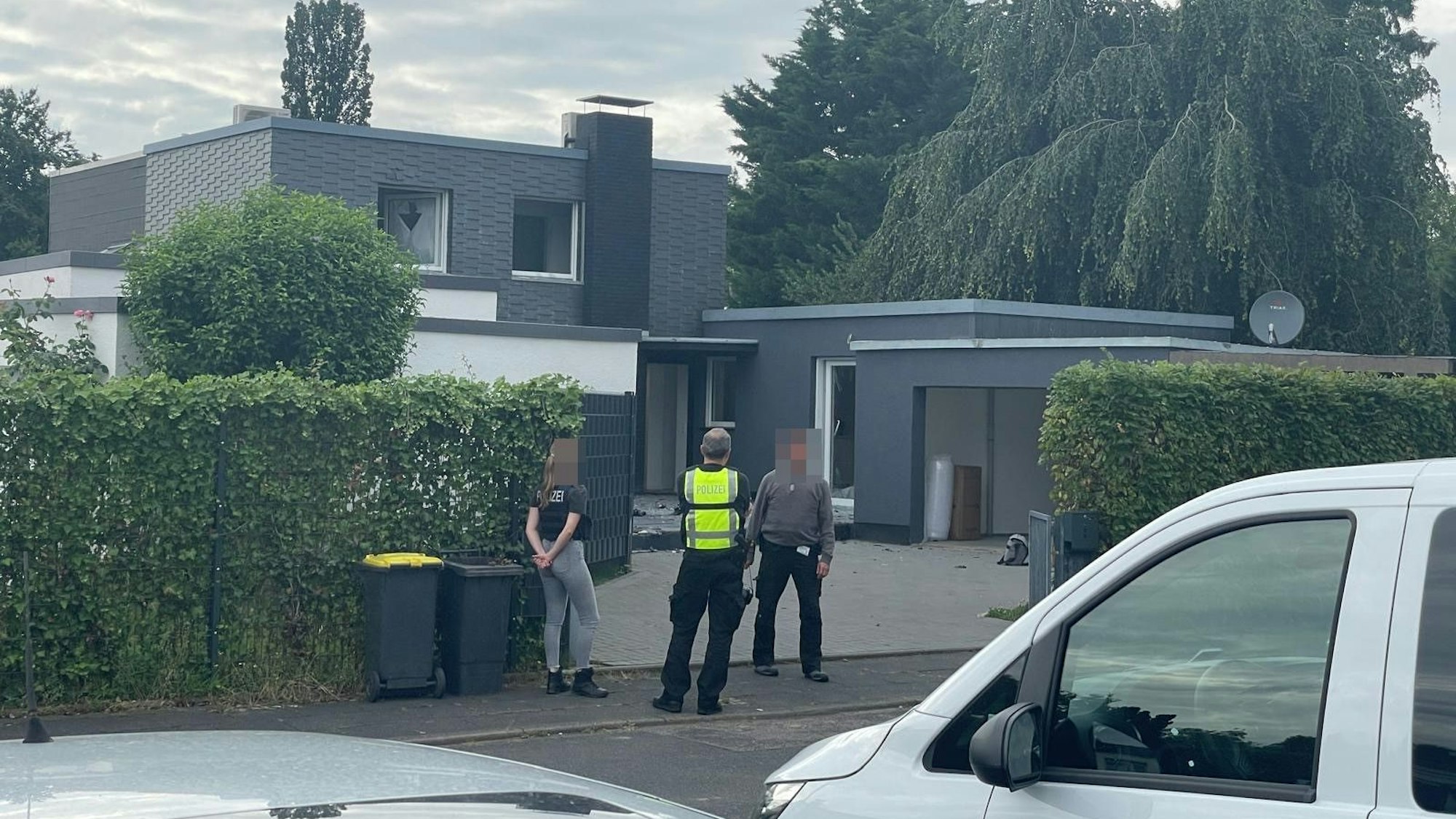 Drei Mitarbeitende der Polizei stehen vor einer Villa.