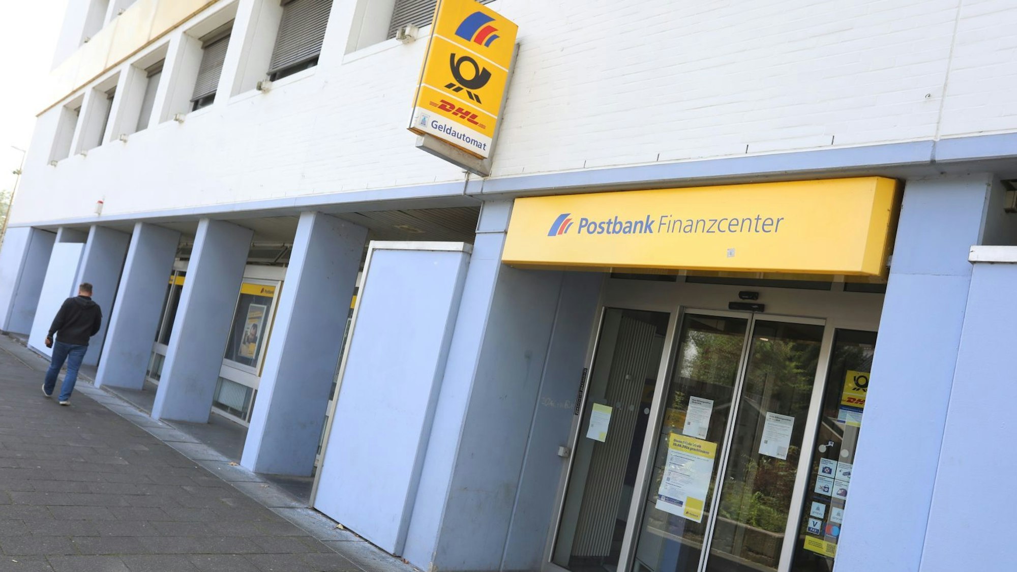 Die Firmenlogos von Postbank und Post an einem Gebäude, an dem ein Mensch vorbeigeht.