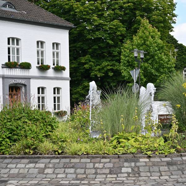 Das Odenthaler Rathaus im Sommer. Davor sprudelt in der Mitte des Kreisverkehrs ein Springbrunnen.