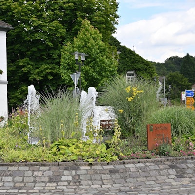 Das Odenthaler Rathaus im Sommer. Davor sprudelt in der Mitte des Kreisverkehrs ein Springbrunnen.