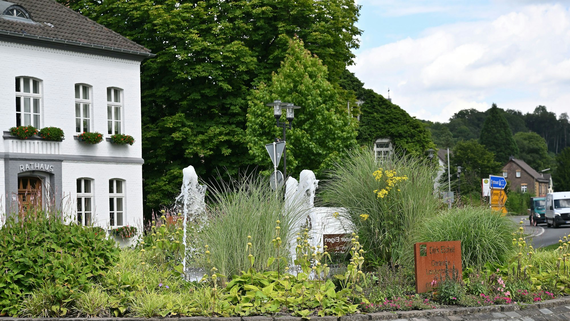 Das Odenthaler Rathaus im Sommer. Davor sprudelt in der Mitte des Kreisverkehrs ein Springbrunnen.