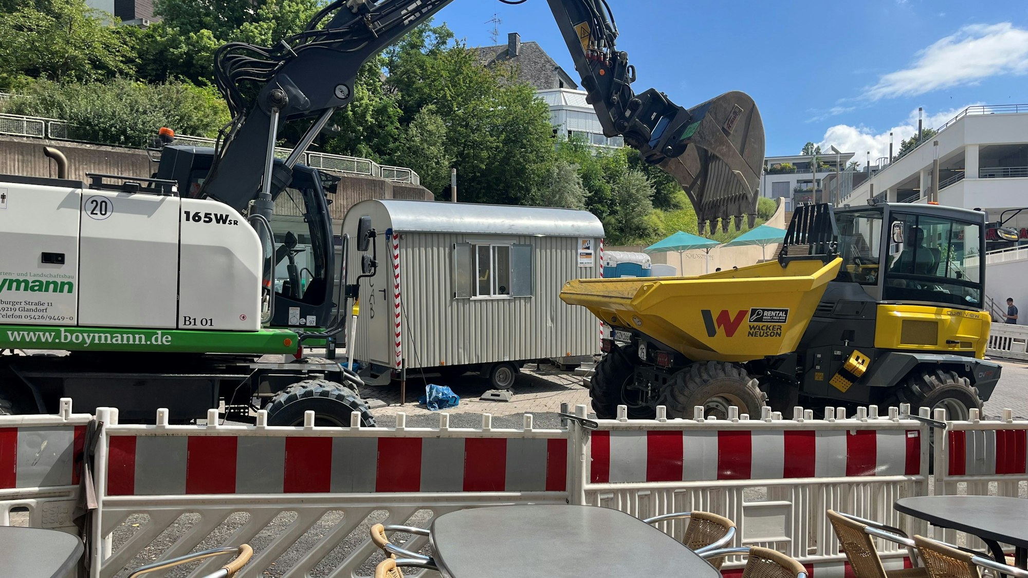 Unmittelbar vor der Absperrung stehen Tische eines Restaurants. Unmittelbar dahinter fährt ein Bagger.