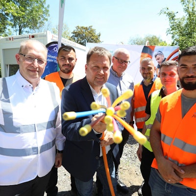 Eine Gruppe von Männern, zum Teil mit Warnwesten gekleidet, halten ein Glasfaserkabel in die Kamera.