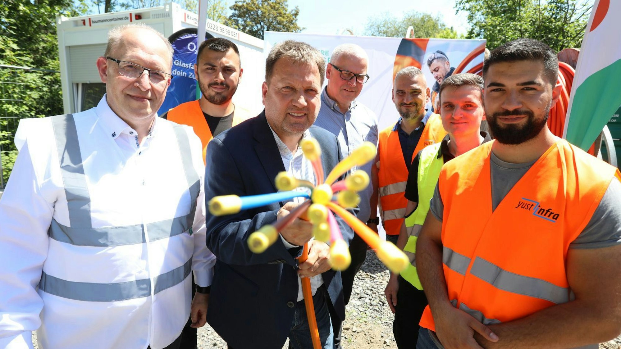 Eine Gruppe von Männern, zum Teil mit Warnwesten gekleidet, halten ein Glasfaserkabel in die Kamera.