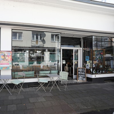 Ein kleines Lokal mit einer großen Fensterfront und Stühlen auf dem Gehweg.