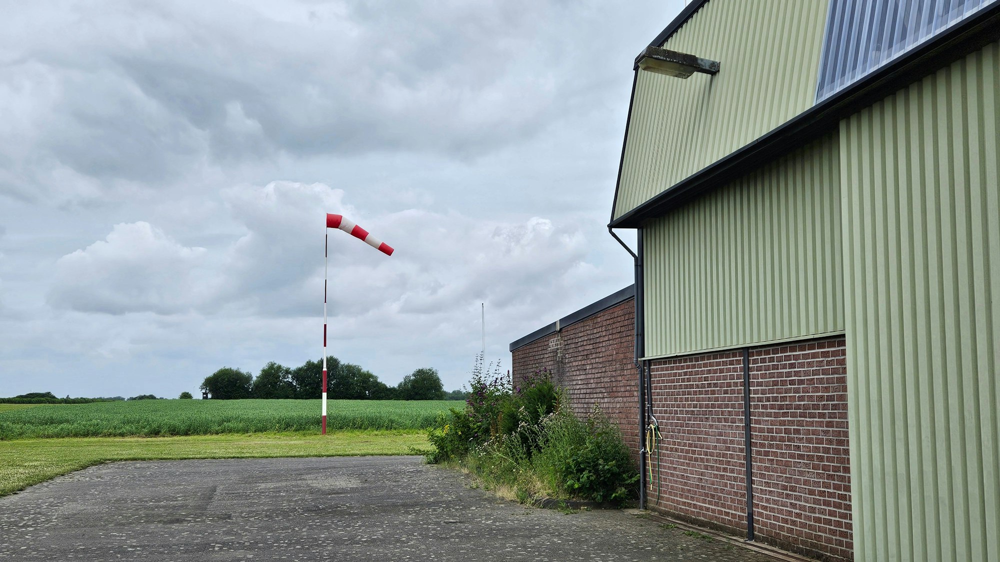 Zu sehen ist eine Halle, neben der ein Windsack steht.