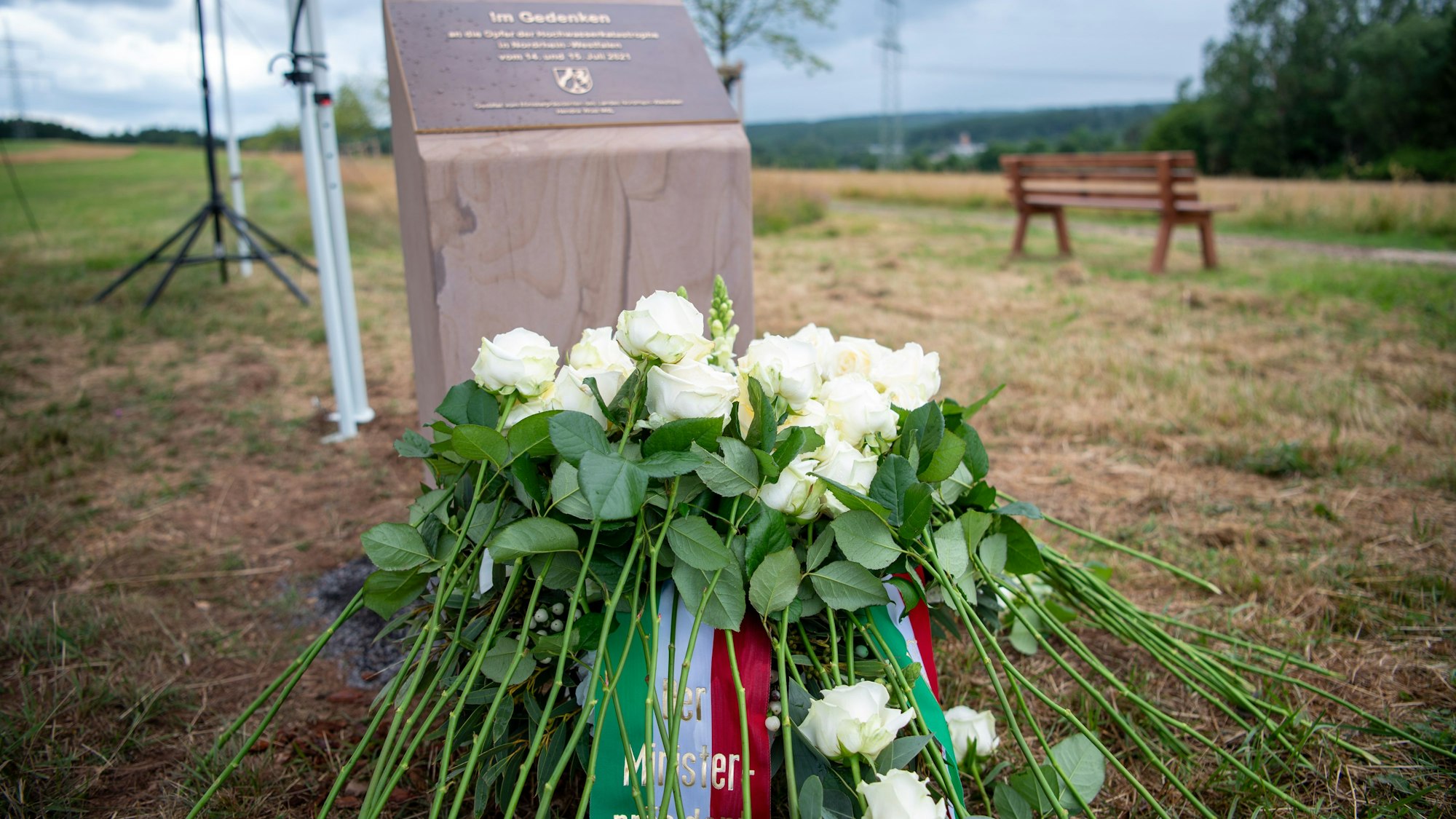 Vor der Gedenkstele liegen ein Kranz und weiße Rosen.