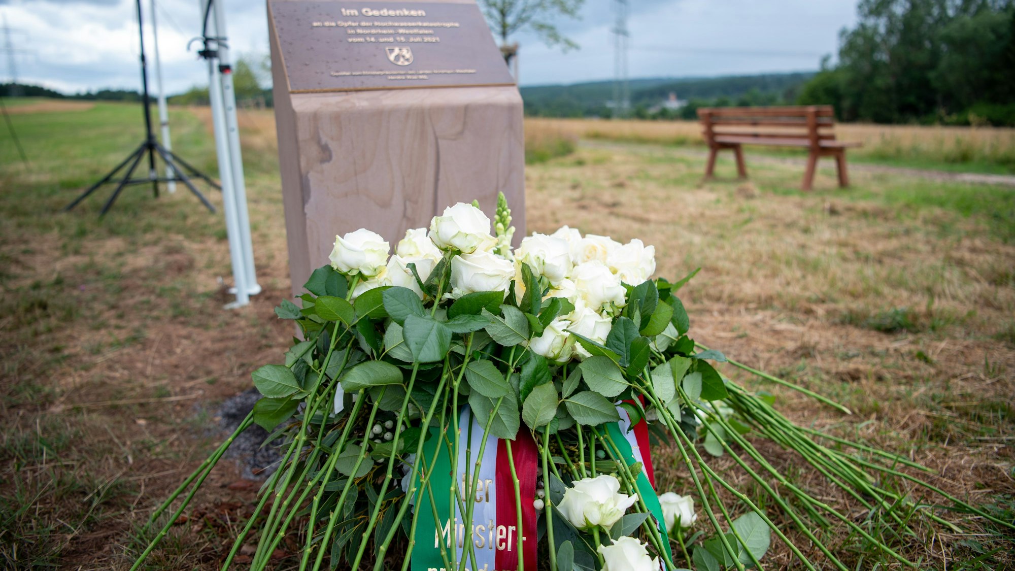 Vor der Gedenkstele liegen ein Kranz und weiße Rosen.