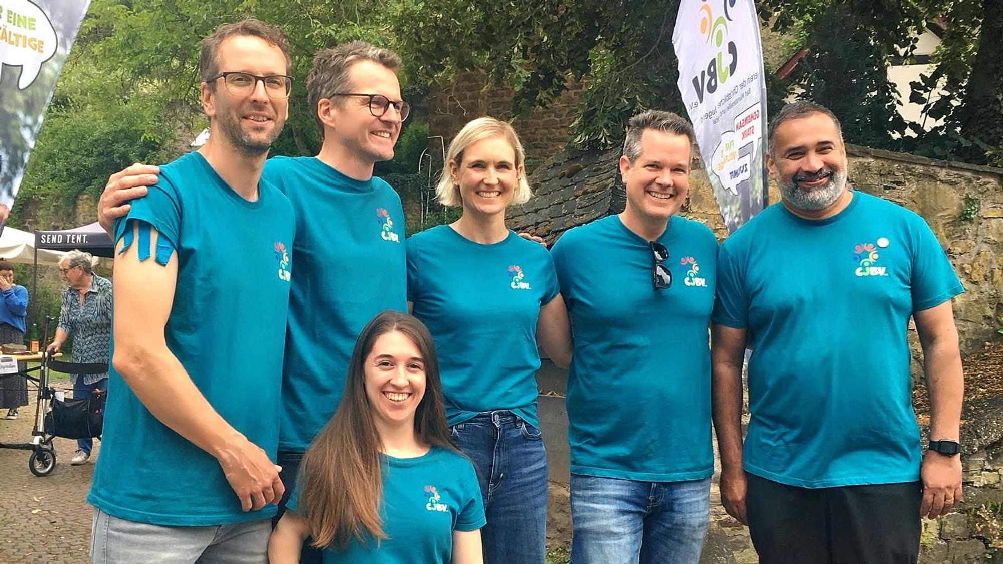 Die Vorstandsmitglieder, in einer Reihe stehend, tragen blaue T-Shirts mit dem Vereinsemblem.