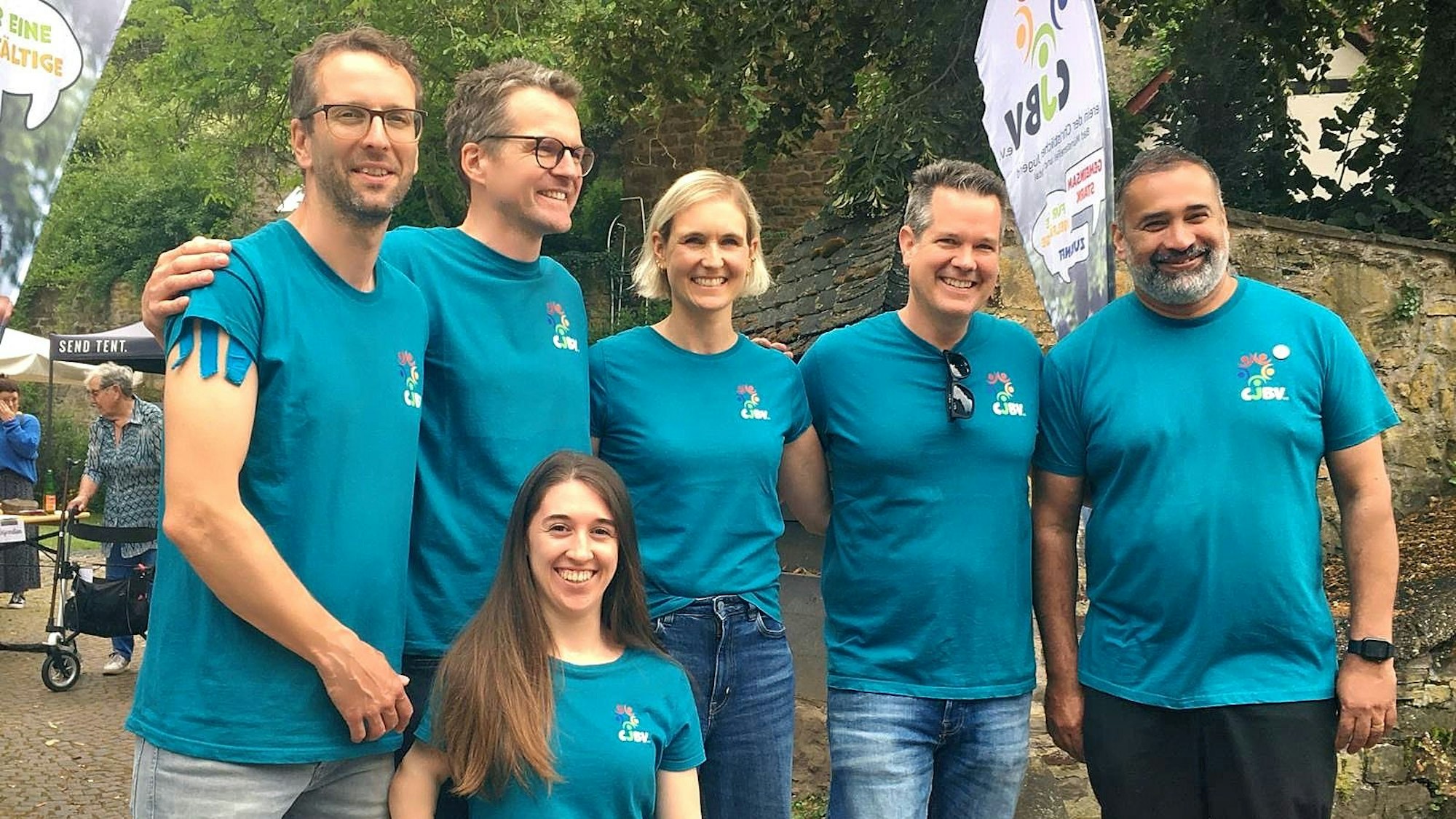 Die Vorstandsmitglieder, in einer Reihe stehend, tragen blaue T-Shirts mit dem Vereinsemblem.