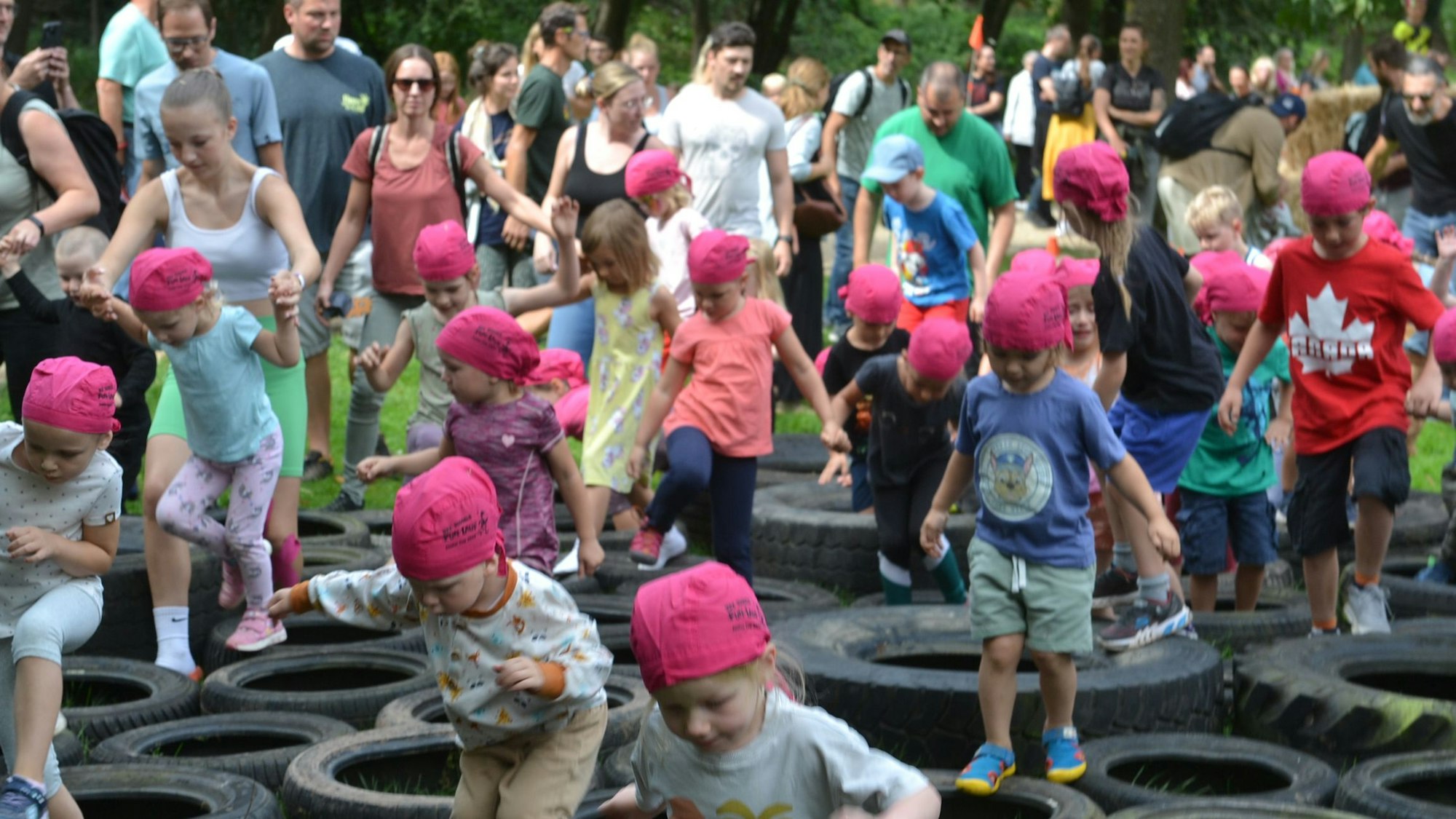 Etliche Kinder, manche unterstützt von ihren Eltern, überwinden eine Hindernis-Station. Sie besteht aus Autoreifen, die flach auf dem Boden liegen.