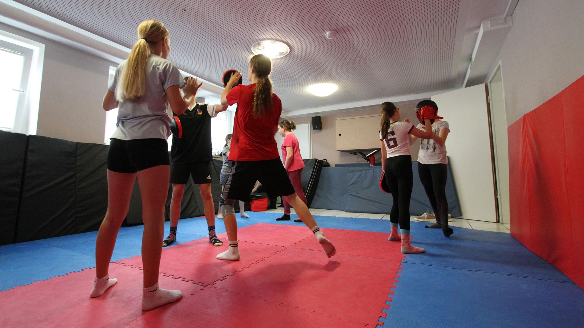 Mädchen beim Kung-Fu in einer mit Matten ausgelegten kleinen Halle.