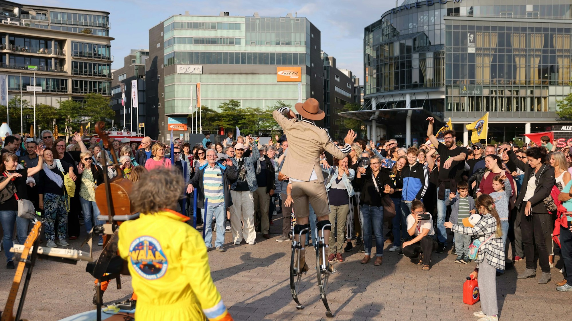 Ein Artist auf Stelzen unterhält eine Menschenmenge auf einem Platz.