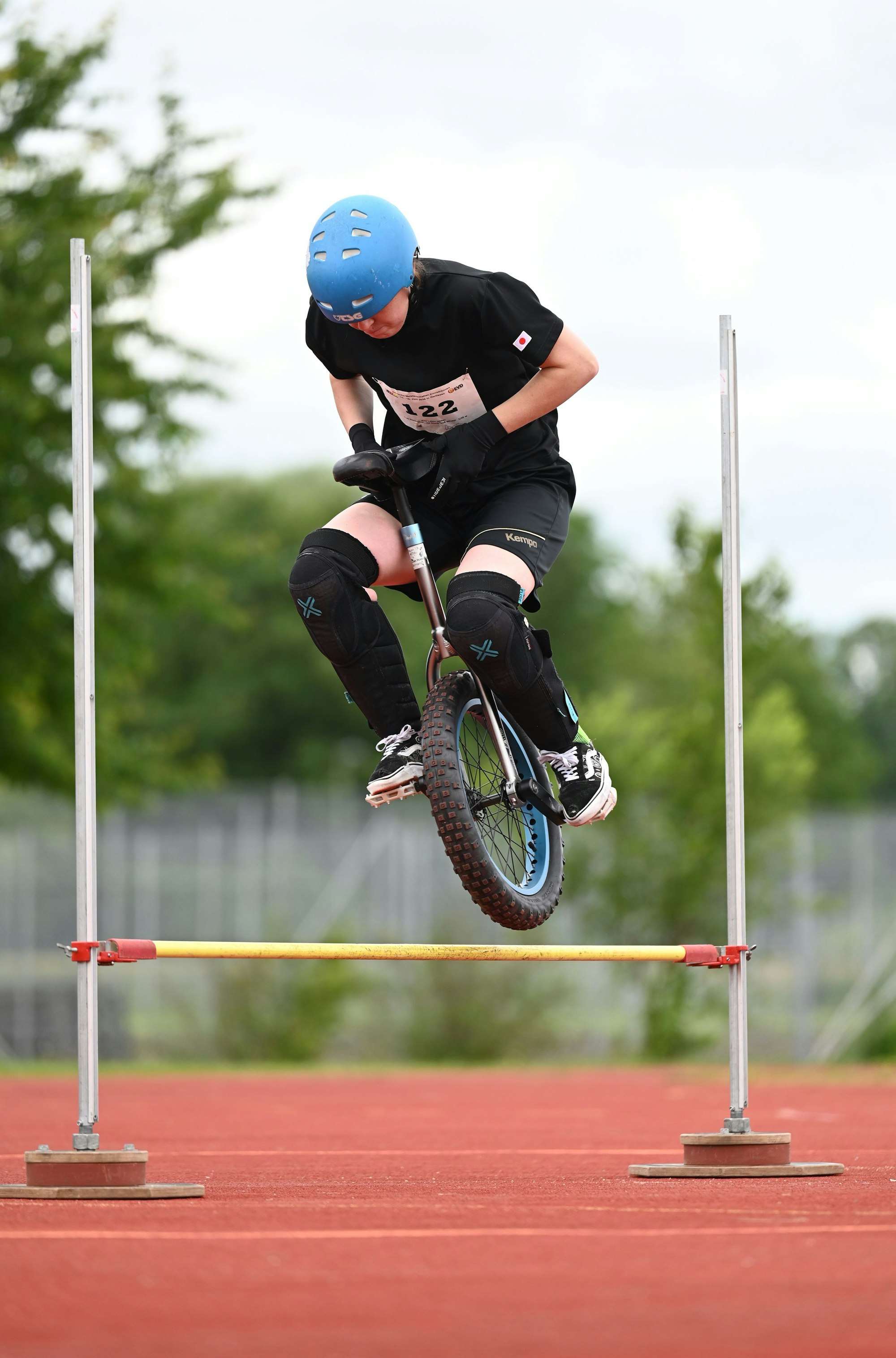 Im Bild ist eine Einradfahrerin, die über ein Hindernis springt.