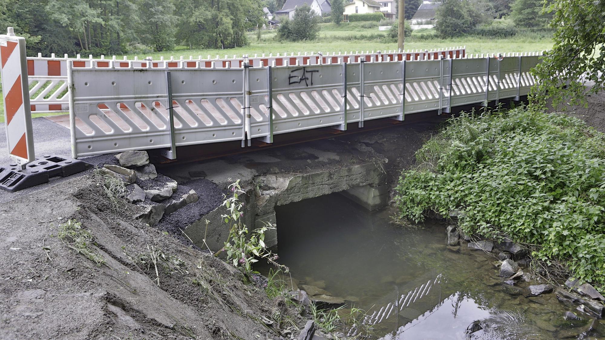 Warnbaken säumen die Fahrbahn auf einer Brücke über einen kleinen Bach.