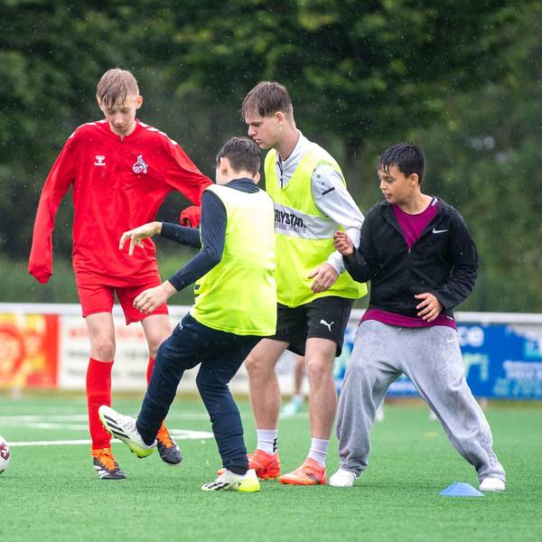 Das Bild zeigt eine Gruppe von Jugendlichen, die auf dem Kunstrasen in Weilerswist im Regen Fußball spielen.