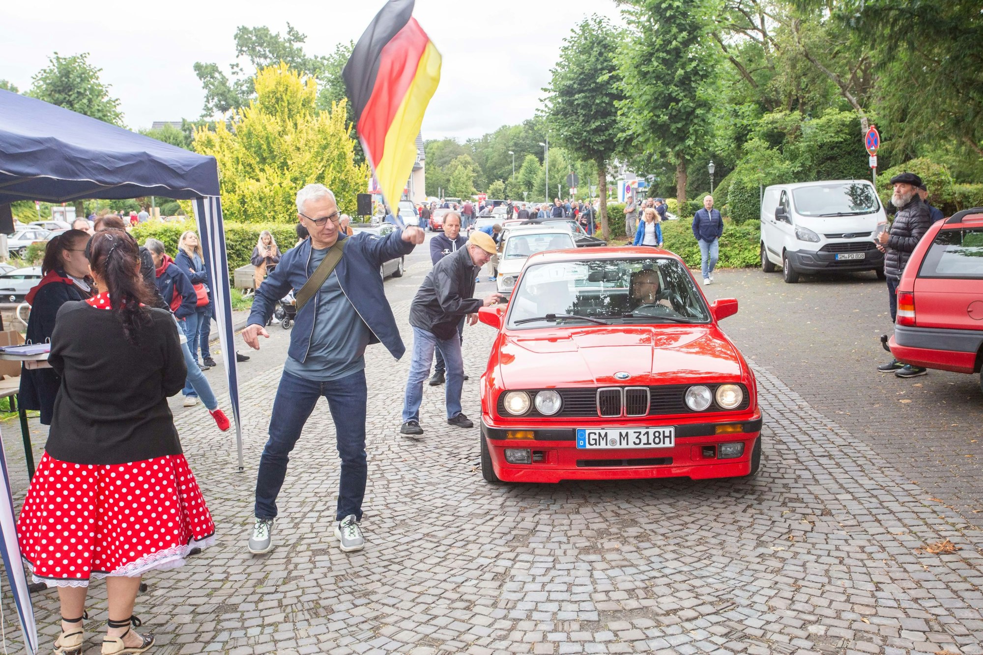 Ein roter BMW geht an den Rallye-Start, eine Deutschland-Fahne gibt das Signal zum Losfahren.