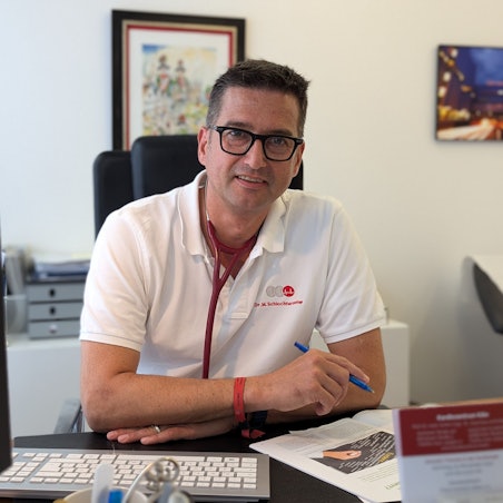 Ein Arzt sitzt an seinem Schreibtisch.