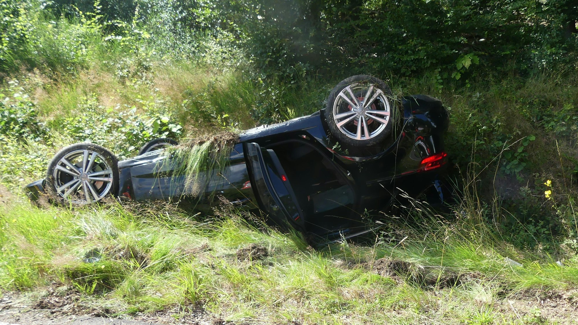 Ein Auto liegt am Straßenrand auf dem Dach.