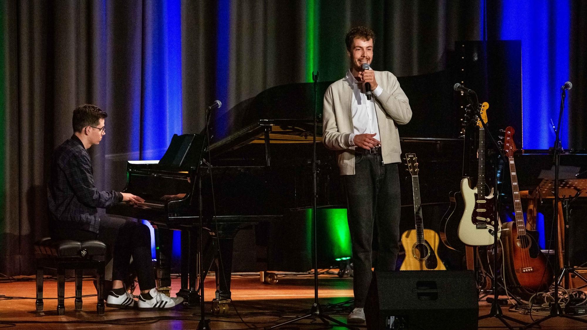 Ein Mann spielt Klavier, der andere lehnt am Flügel und singt in ein Mikrofon.