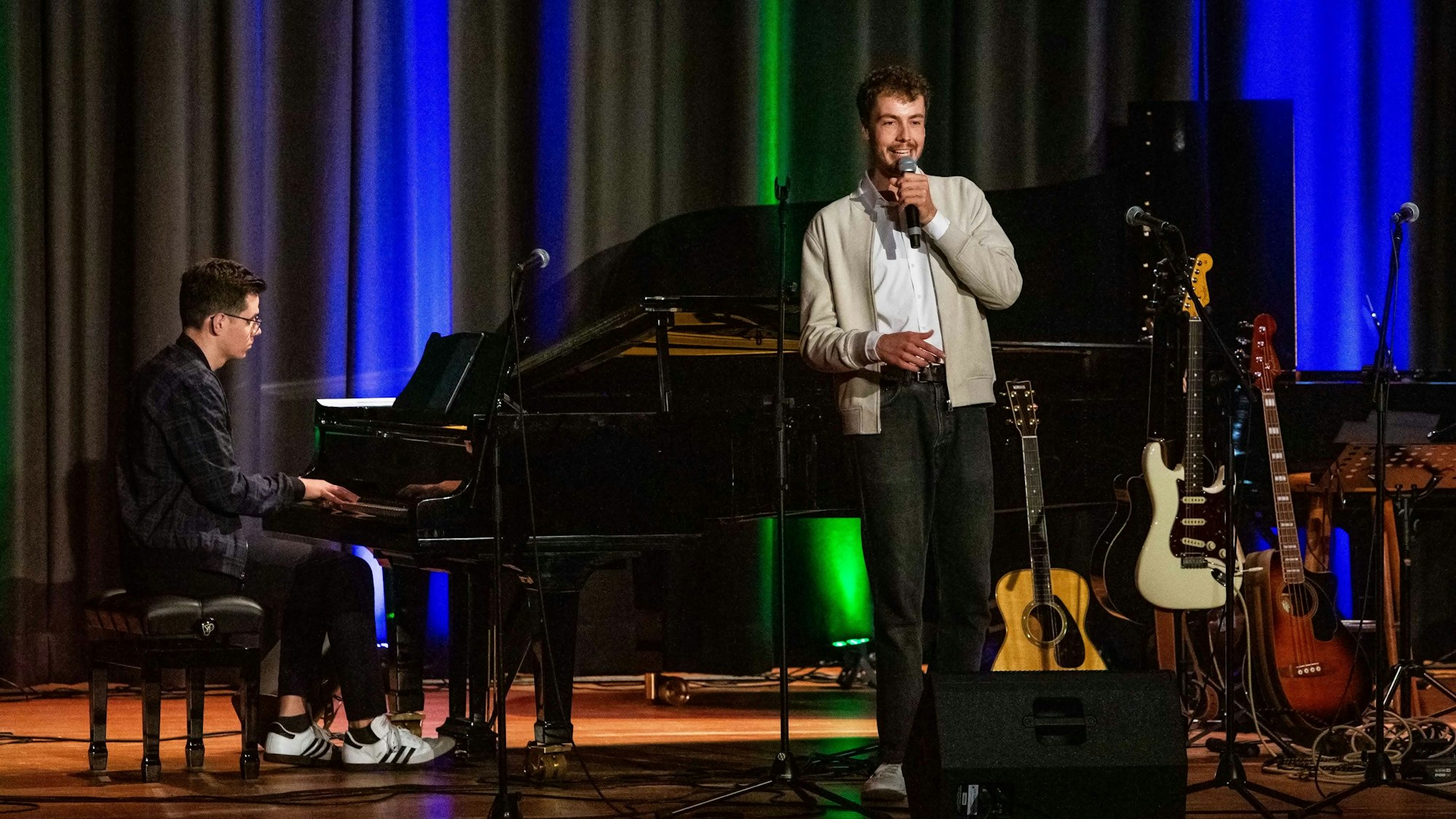 Ein Mann spielt Klavier, der andere lehnt am Flügel und singt in ein Mikrofon.