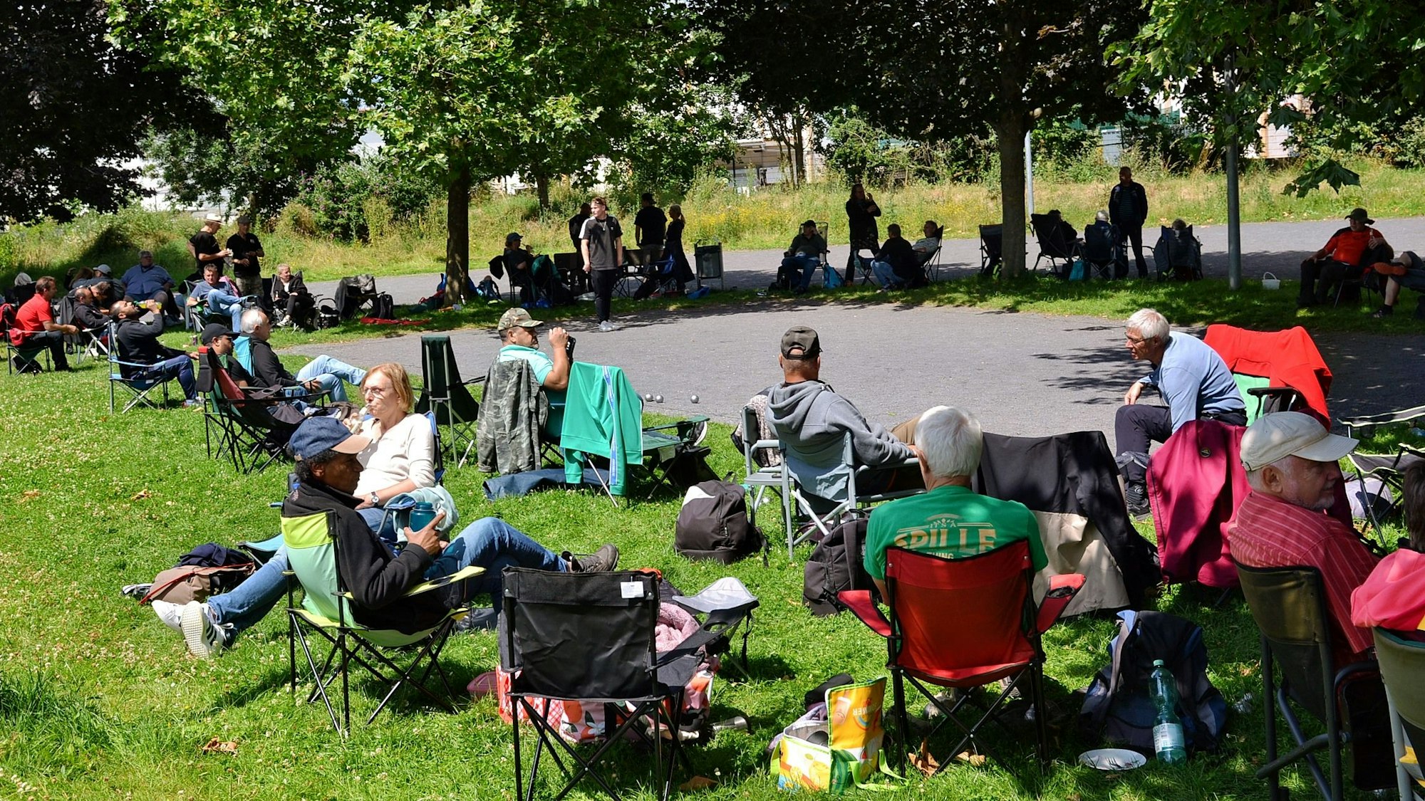 Die Teilnehmer und Besucher des Boule-Turniers in Euskirchen sitzen auf Campingstühlen rund um den Platz.