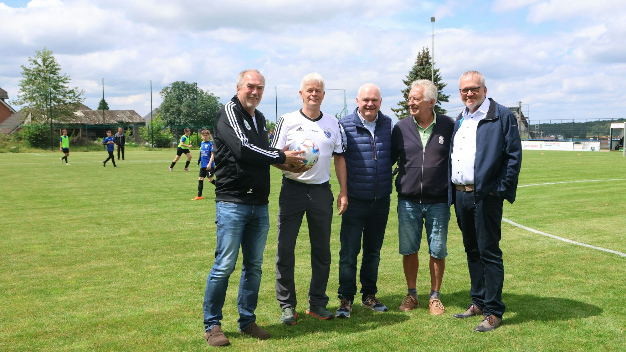 Die vier Männer stehen auf dem neuen Rasenplatz.