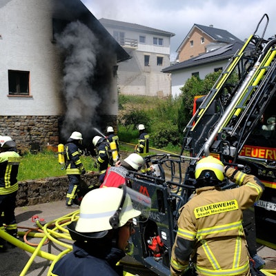 Zahlreiche Feuerwehrleute löschen den Brand in einem Haus in Nettersheim. Aus der Garage im Keller quillt dichter, schwarzer Rauch