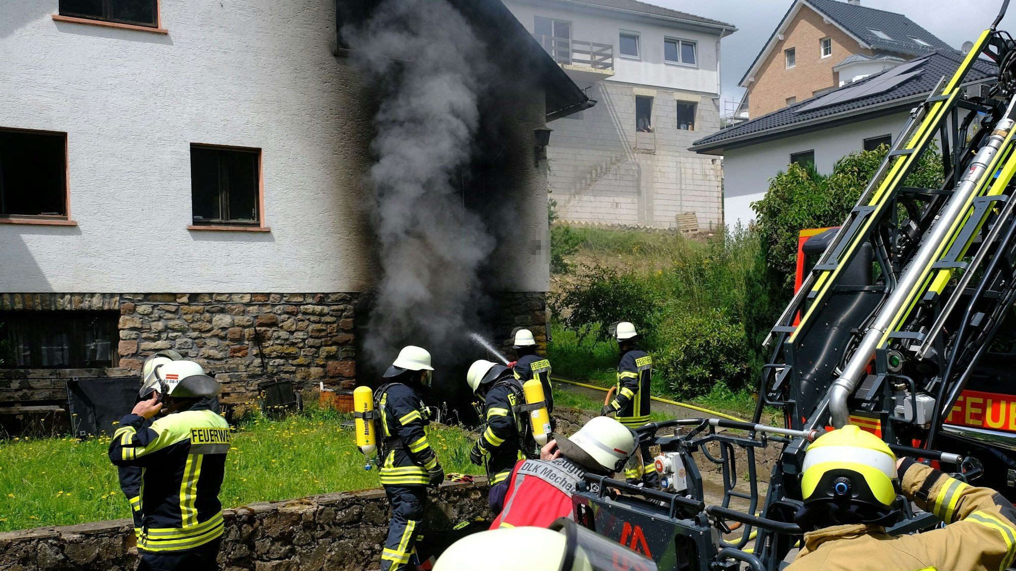 Zahlreiche Feuerwehrleute löschen den Brand in einem Haus in Nettersheim. Aus der Garage im Keller quillt dichter, schwarzer Rauch