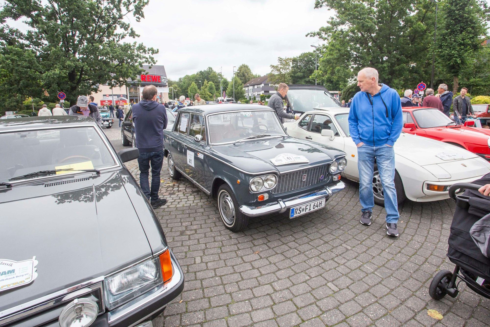 Oldtimer stehen auf einem Platz, Menschen schauen sich die Autos an.