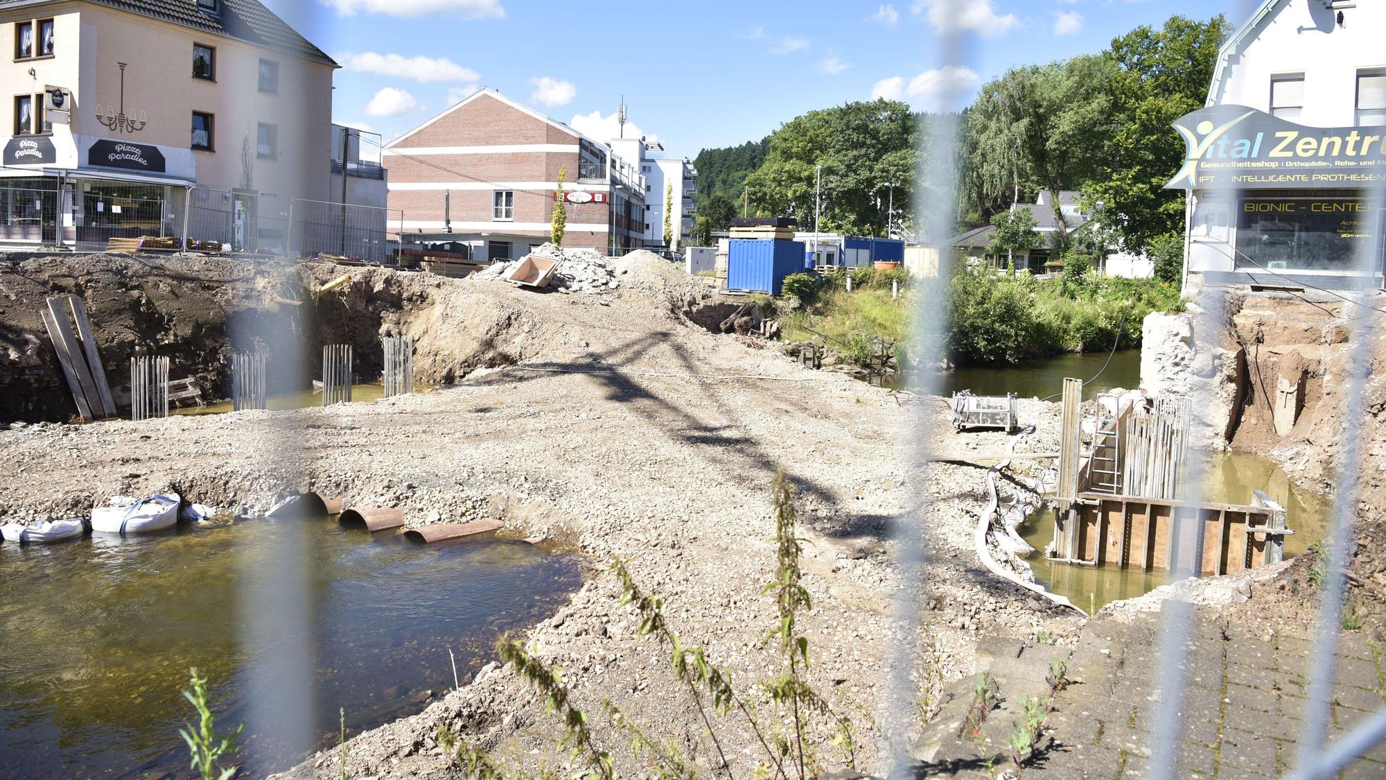 Durch einen Baustellenzaun hindurch sieht man eine Baustelle auf einem Fluss. Links und rechts sind Häuser.