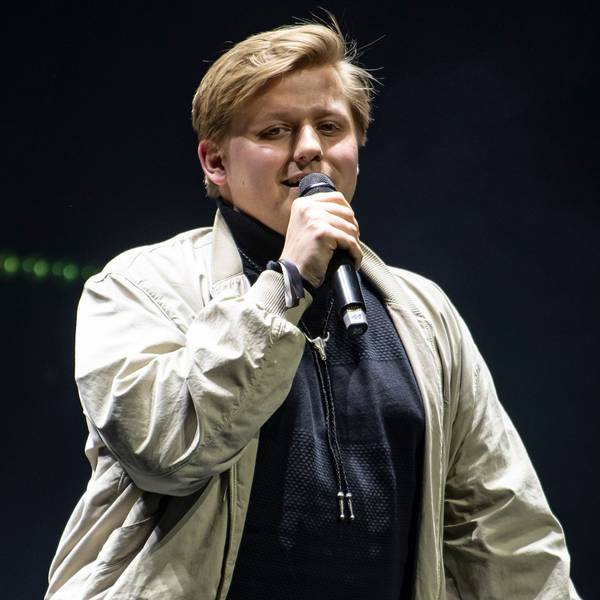 Autot Sebastian „El Hotzo“ Hotz steht auf einer Bühne und spricht in ein Mikrofon.