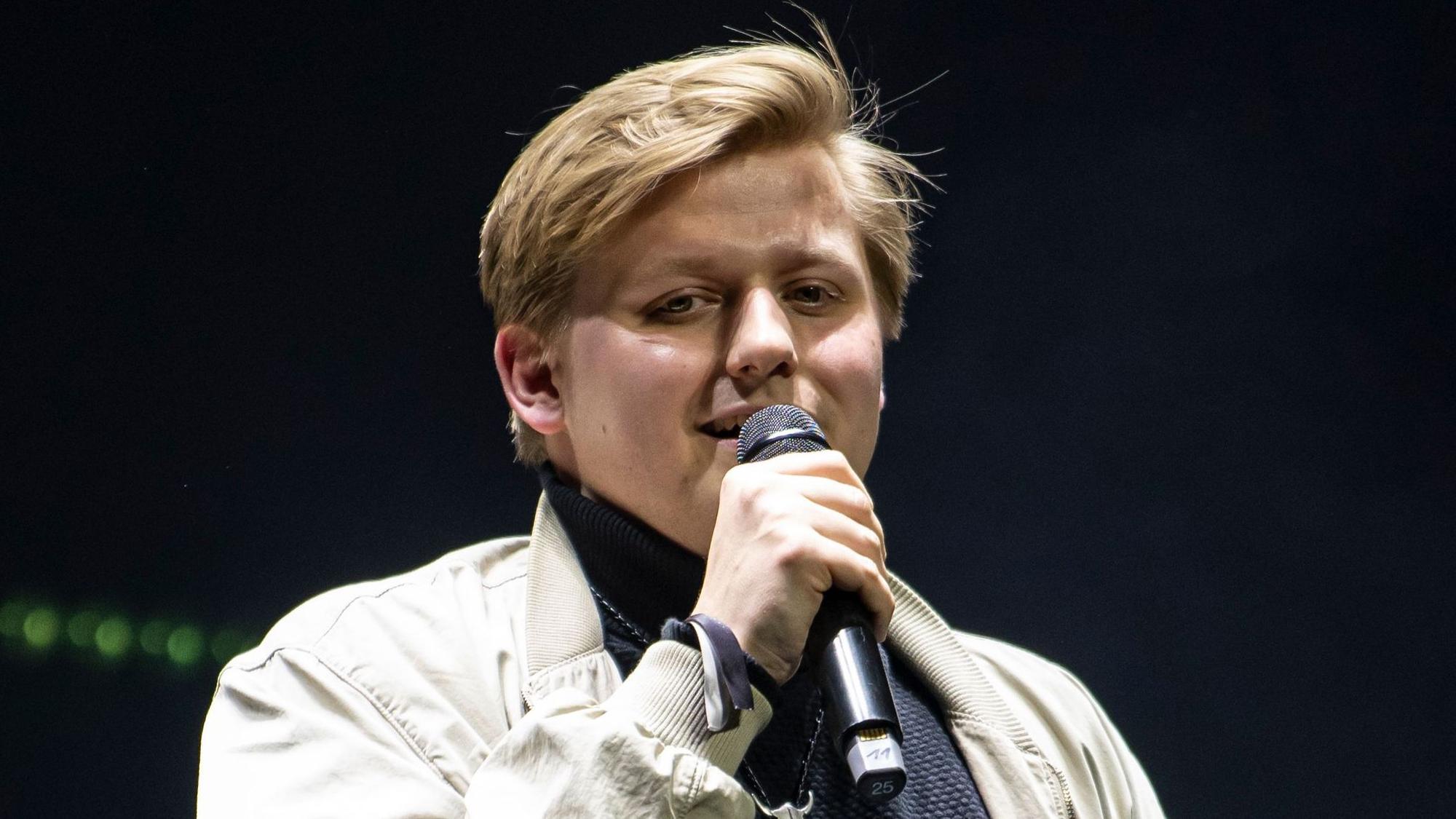 Autot Sebastian „El Hotzo“ Hotz steht auf einer Bühne und spricht in ein Mikrofon.