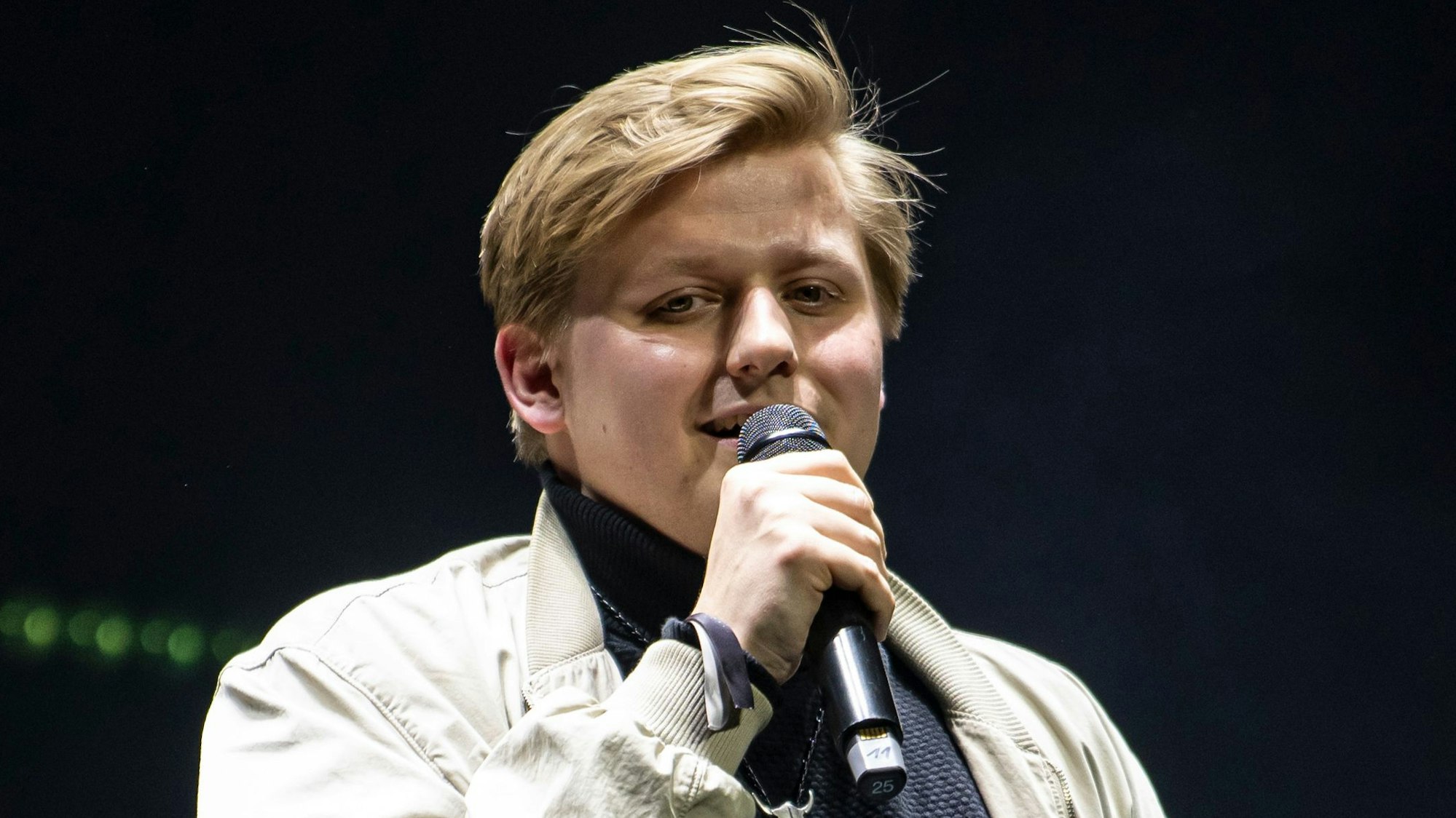 Autot Sebastian „El Hotzo“ Hotz steht auf einer Bühne und spricht in ein Mikrofon.