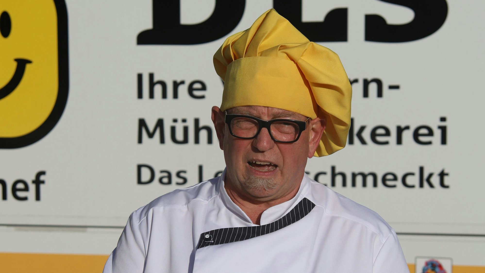 Ein Mann mit einer dunklen Brille und einer gelben Kochmütze auf dem Kopf.