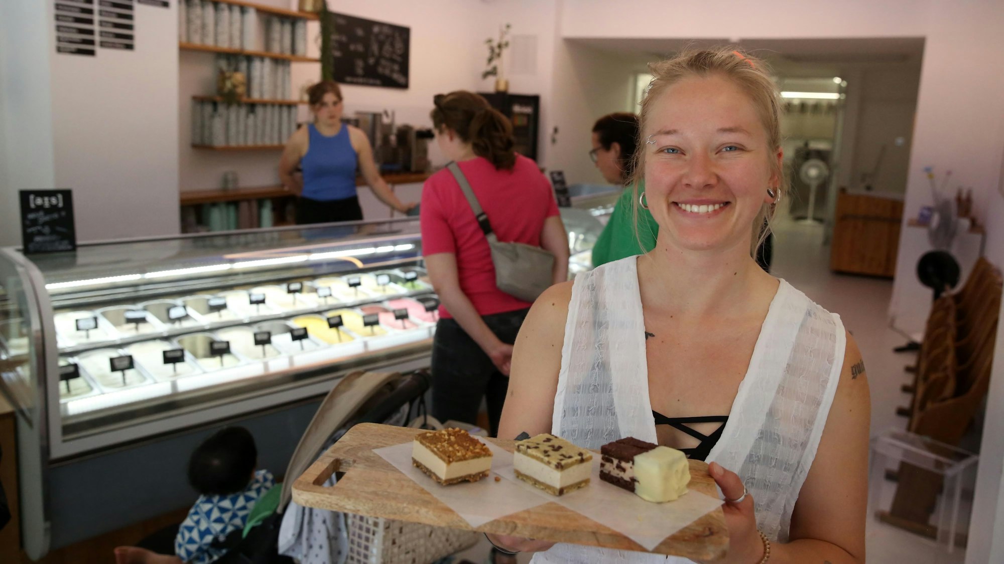 Eine Frau hält ein Brettchen mit mehreren Eisschnitten drauf. Im Hintergrund ist eine Eistheke zu sehen.