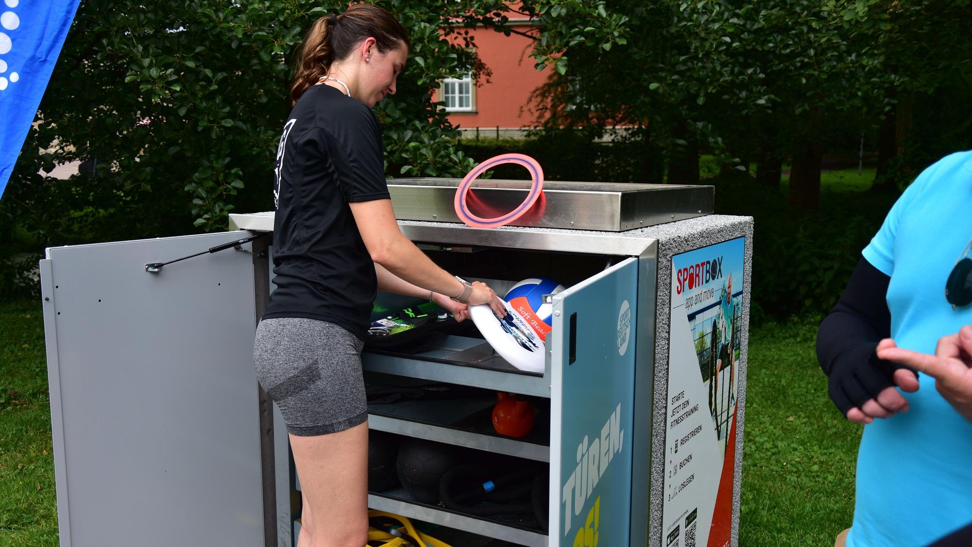 Eine Sportlerin hat die Sportbox an Burg Wissen geöffnet und sucht sich ein Sportgerät aus.