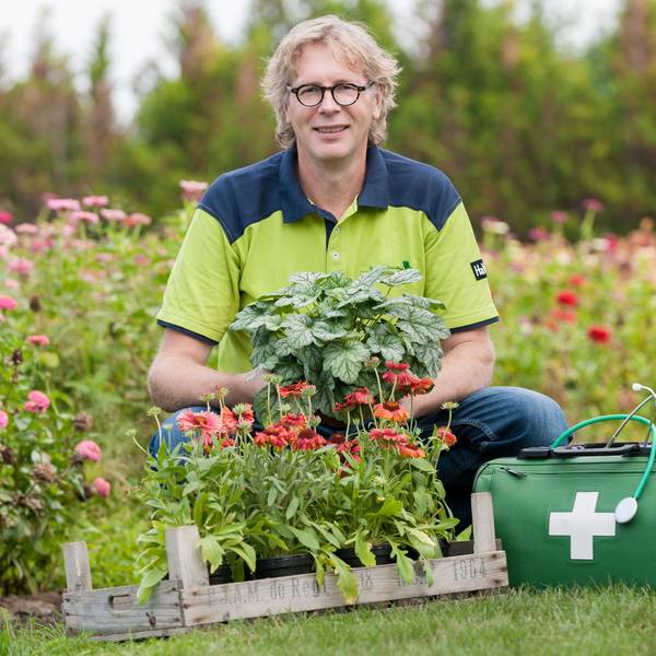 René Wadas posiert neben einem Arztkoffer inmitten blühender Blumen.