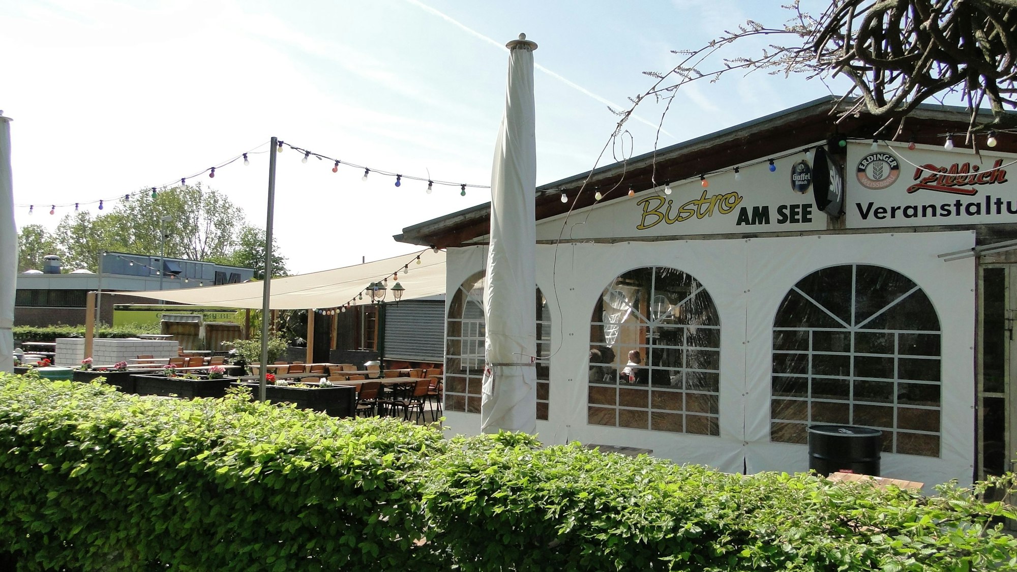 Der Außenbereich mit Stühlen, Tischen und Lichterketten des Biergarten „Bistro am See“.