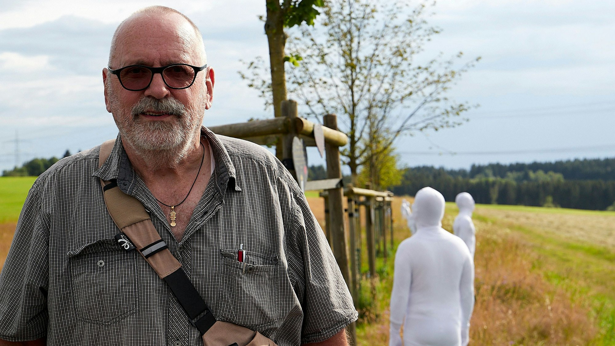 Klaus Jansen aus Odendorf steht an der zentralen Flut-Gedenkstätte des Landes NRW. Hinter ihm sind Teilnehmer einer Kunstaktion in weißen Anzügen zu sehen.