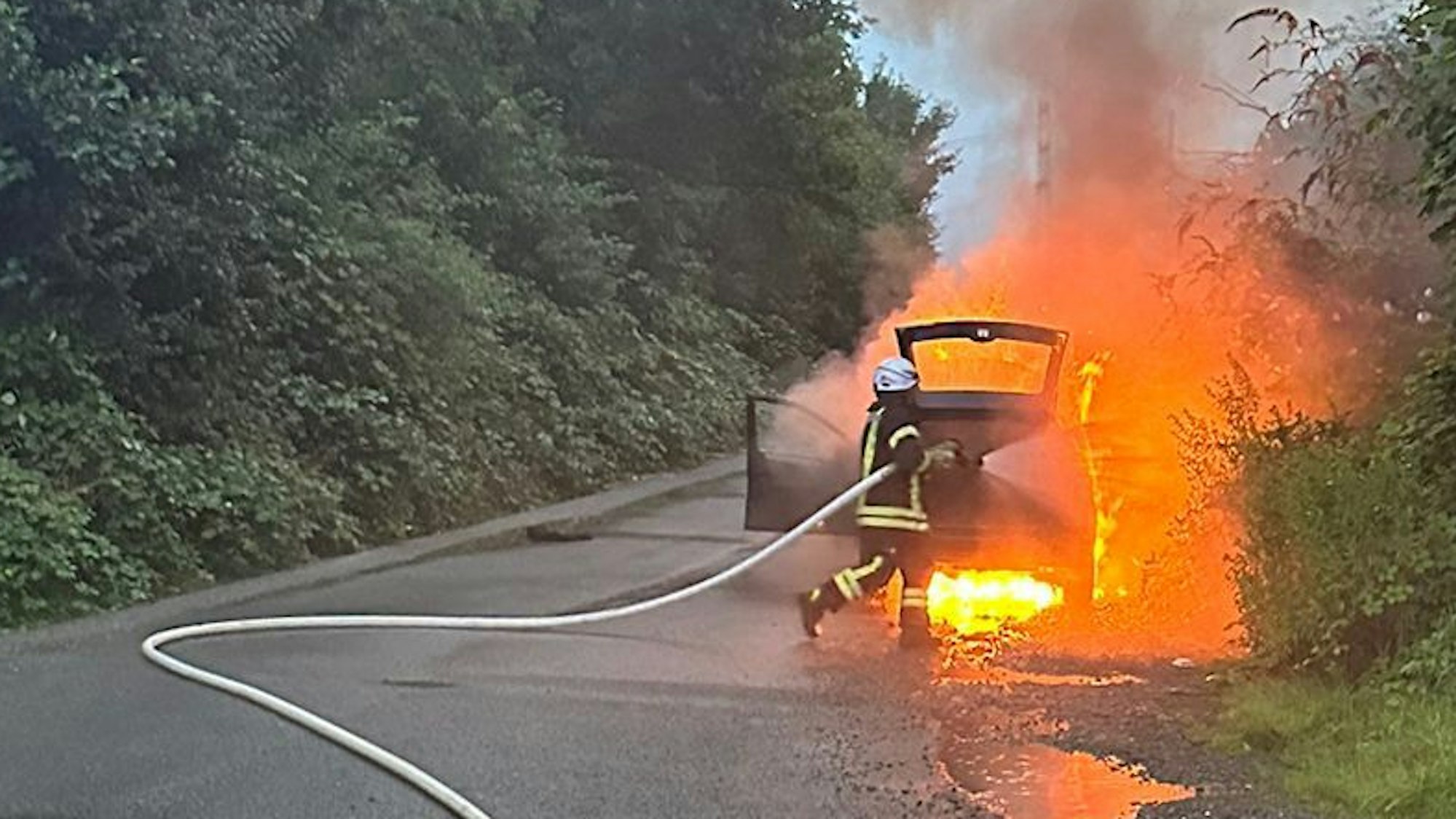 Ein Feuerwehrmann richtet einen Schlauch auf ein brennendes Auto.