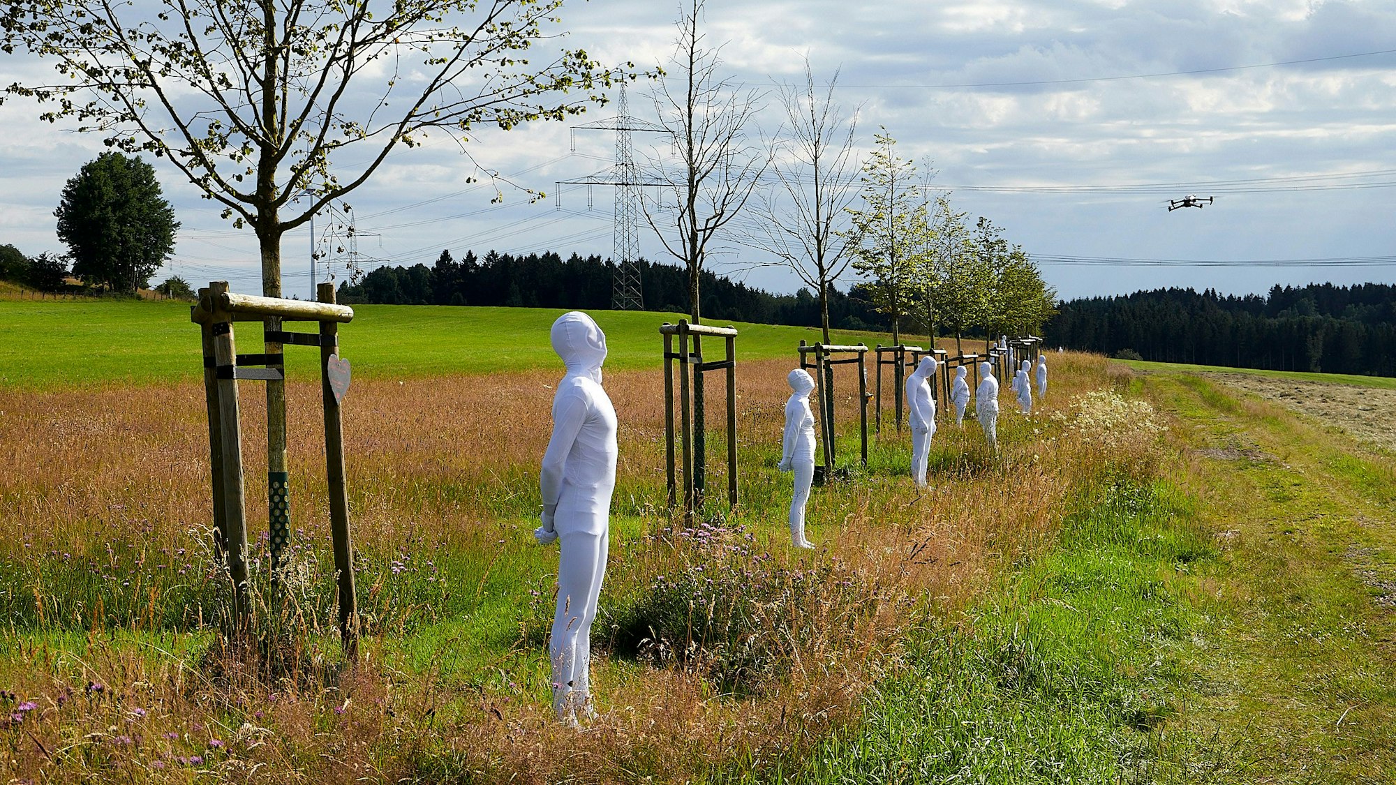 In weiße Anzüge gekleidete Menschen stehen vor den Bäumen der zentralen NRW-Gedenkstätte für die Opfer der Flutkatastrophe. Sie symbolisieren die gestorbenen Menschen.