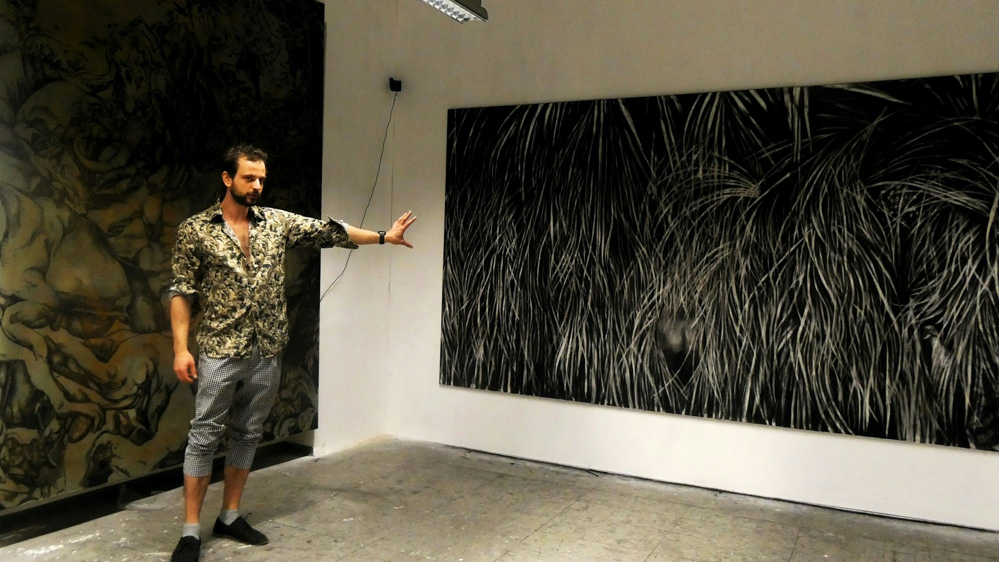 Ein junger Mann steht vor zwei düster wirkenden, großen Bildern.